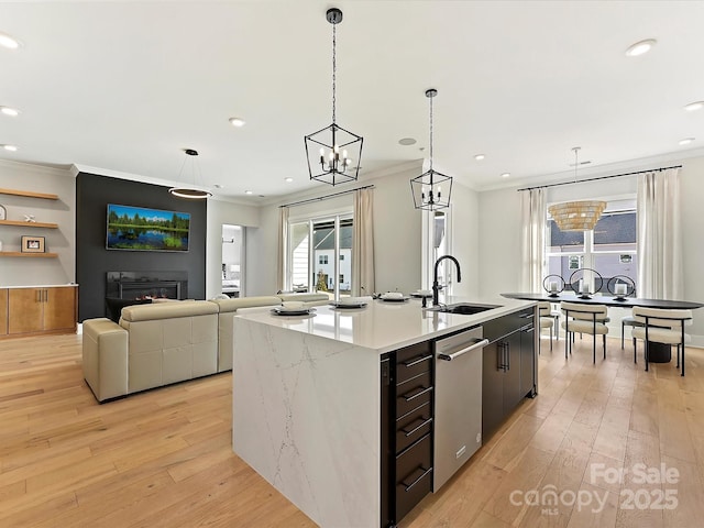 kitchen with pendant lighting, light countertops, open floor plan, a sink, and an island with sink