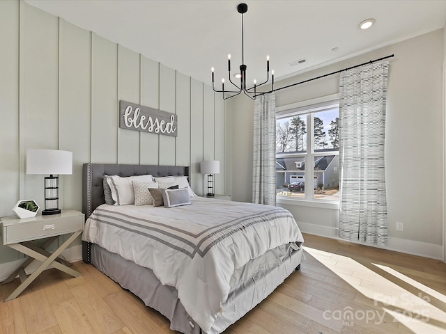 bedroom with baseboards, light wood-type flooring, visible vents, and an inviting chandelier