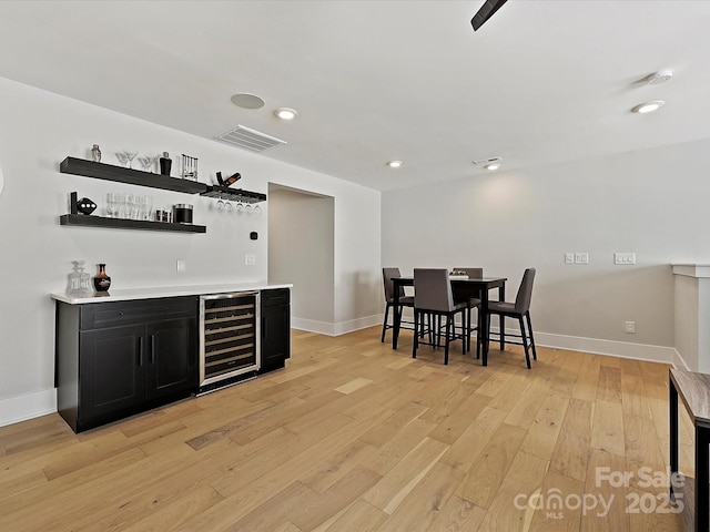 bar with a dry bar, visible vents, light wood-type flooring, beverage cooler, and baseboards