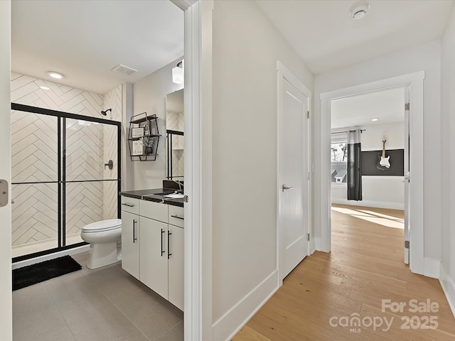 bathroom featuring visible vents, toilet, vanity, wood finished floors, and baseboards