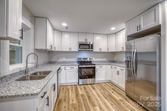 kitchen featuring white cabinets, light stone countertops, stainless steel appliances, light wood-type flooring, and a sink