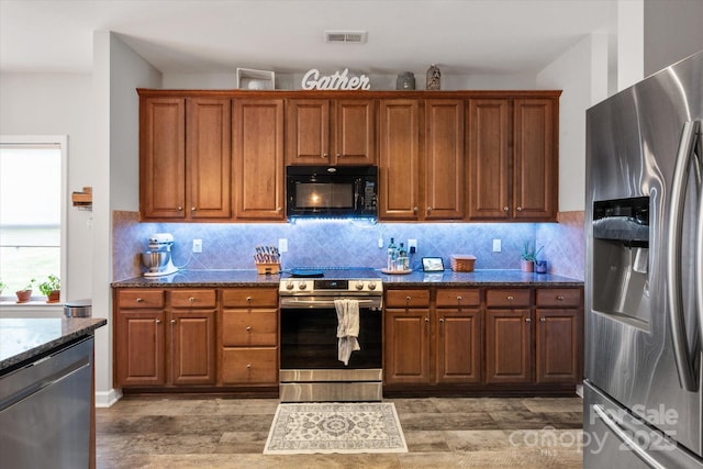 3216 Bridgewick Rd, Waxhaw, NC 28173 - kitchen with stainless steel appliances, brown cabinets, light wood-style floors, and dark stone countertops