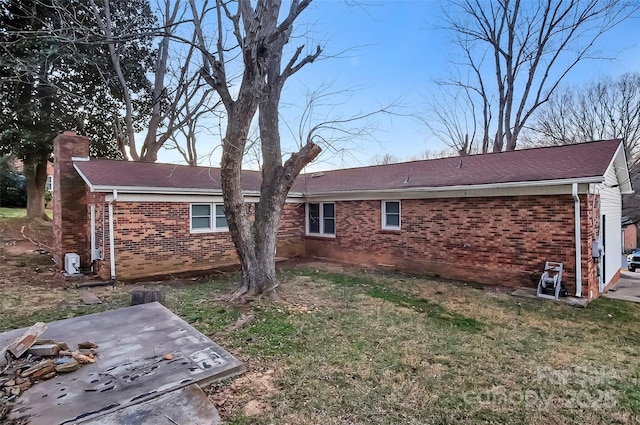 rear view of property featuring roof with shingles, a chimney, a lawn, and brick siding