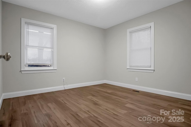 spare room featuring visible vents, baseboards, and wood finished floors