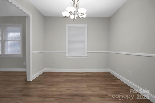 unfurnished dining area with visible vents, a notable chandelier, baseboards, and wood finished floors