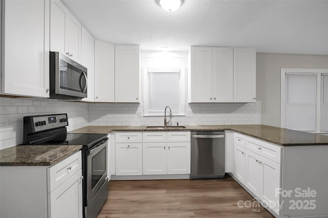 kitchen with white cabinets, appliances with stainless steel finishes, wood finished floors, a peninsula, and a sink