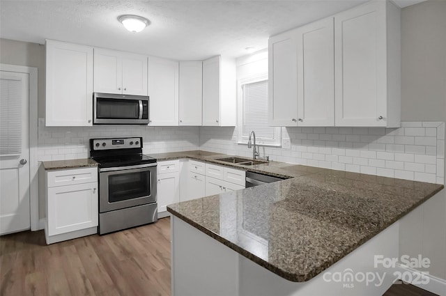 kitchen with appliances with stainless steel finishes, white cabinetry, a sink, dark stone countertops, and light wood-type flooring