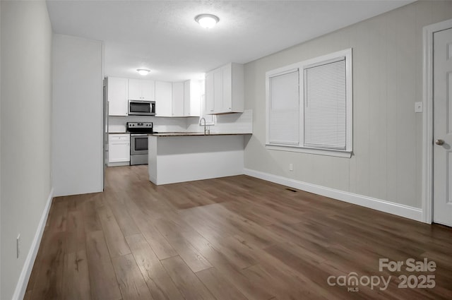 kitchen with baseboards, dark wood finished floors, appliances with stainless steel finishes, a peninsula, and white cabinetry