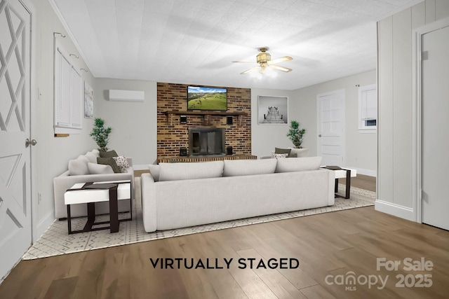 living area featuring a brick fireplace, wood finished floors, a ceiling fan, and a wall mounted air conditioner