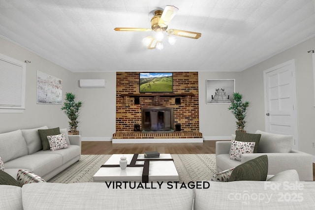 living room with a brick fireplace, a wall unit AC, baseboards, and wood finished floors