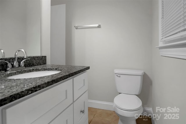 half bathroom with tile patterned flooring, baseboards, vanity, and toilet