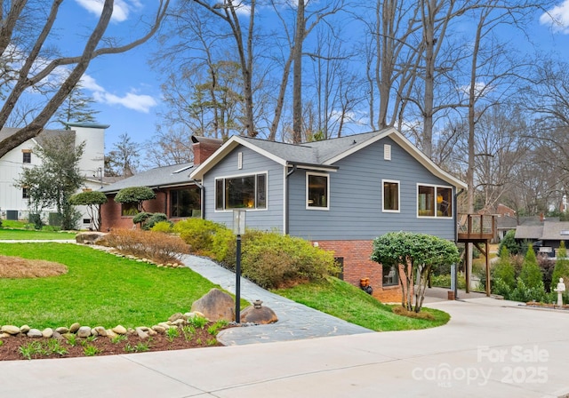 view of front facade featuring concrete driveway, brick siding, a front yard, and a chimney