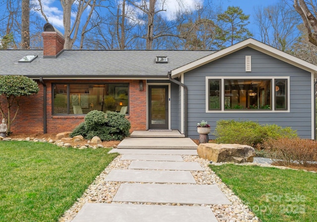 view of front facade featuring a front lawn, brick siding, a chimney, and a shingled roof