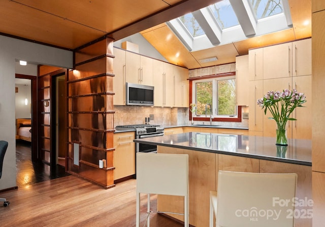 kitchen featuring a sink, decorative backsplash, light wood-style floors, appliances with stainless steel finishes, and lofted ceiling with skylight