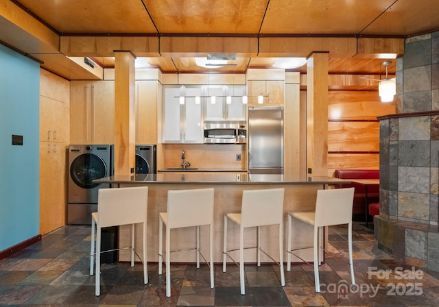 kitchen with a kitchen bar, a sink, white cabinetry, stainless steel appliances, and washer / dryer