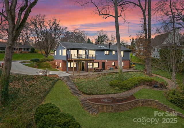 back of house featuring a deck, a patio, a yard, brick siding, and a chimney