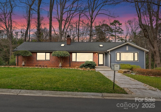 view of front of property with a yard, brick siding, roof with shingles, and a chimney