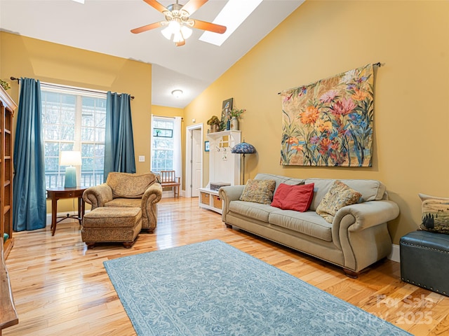 living room with high vaulted ceiling, a skylight, light hardwood / wood-style floors, and ceiling fan