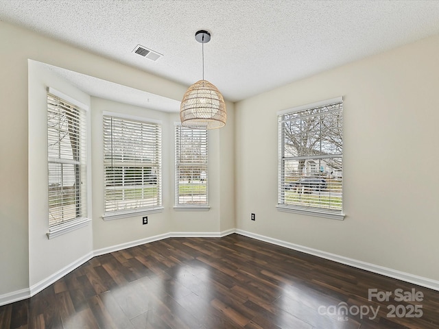 unfurnished dining area featuring dark wood-style floors, visible vents, a textured ceiling, and baseboards