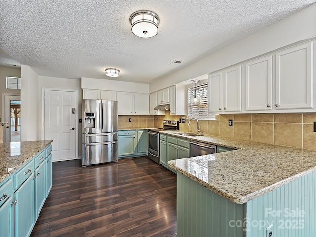 kitchen with appliances with stainless steel finishes, white cabinets, a sink, and light stone counters