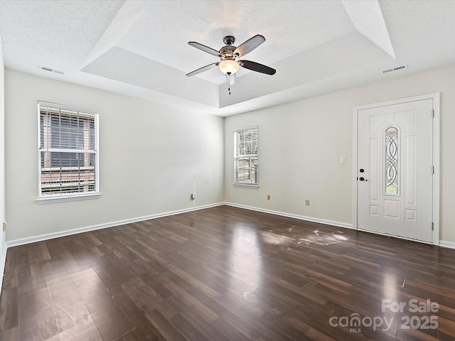 interior space with visible vents, a tray ceiling, dark wood finished floors, and a textured ceiling