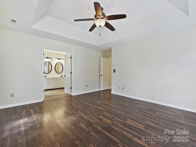 empty room featuring baseboards, visible vents, a raised ceiling, a ceiling fan, and dark wood-style floors