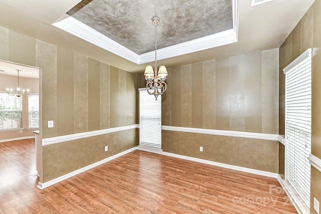 unfurnished room with an inviting chandelier, hardwood / wood-style floors, a tray ceiling, and ornamental molding