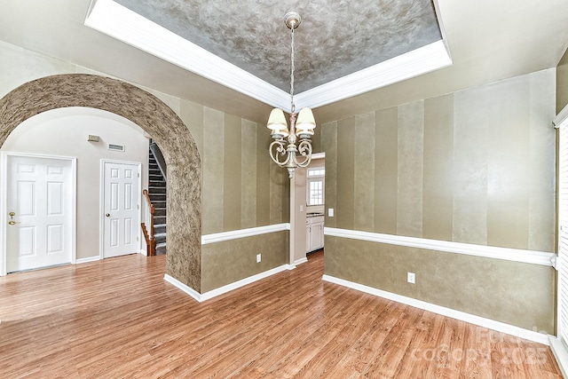 spare room featuring a tray ceiling, wood-type flooring, and a chandelier