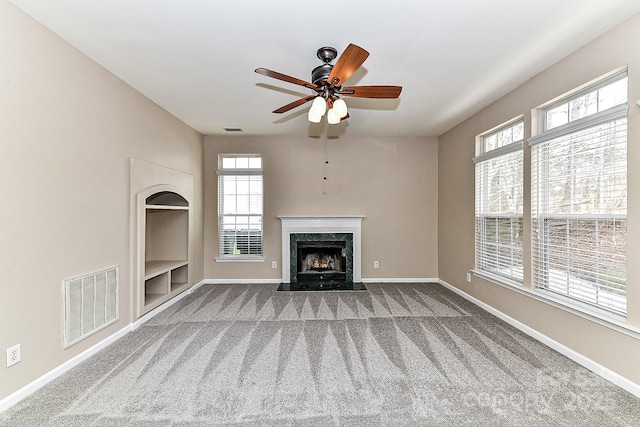 unfurnished living room with built in shelves, a high end fireplace, ceiling fan, and carpet flooring