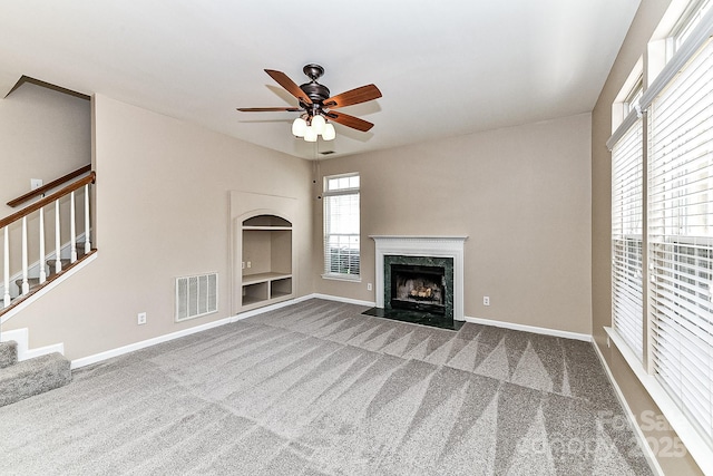 unfurnished living room with a high end fireplace, carpet floors, and ceiling fan