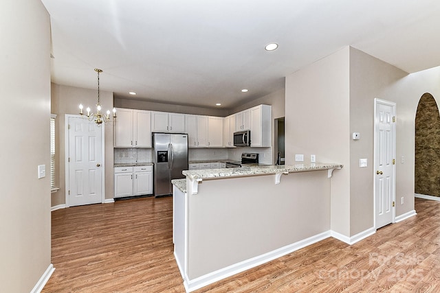 kitchen featuring light wood-type flooring, kitchen peninsula, white cabinets, and appliances with stainless steel finishes