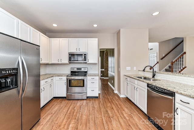 kitchen with sink, light wood-type flooring, appliances with stainless steel finishes, light stone countertops, and white cabinets