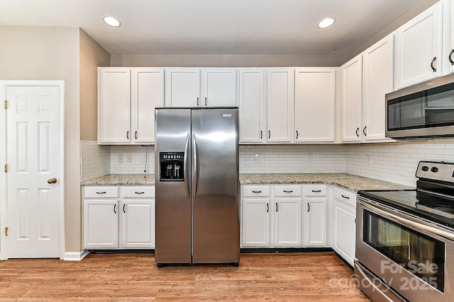 kitchen with white cabinetry, appliances with stainless steel finishes, light stone counters, and light hardwood / wood-style flooring