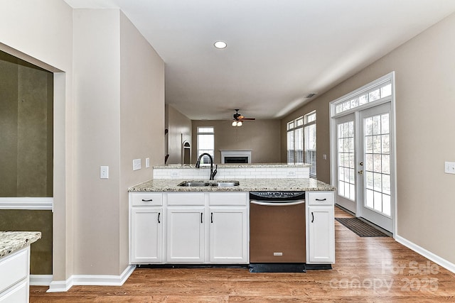 kitchen featuring sink, light stone counters, light wood-type flooring, dishwashing machine, and white cabinets