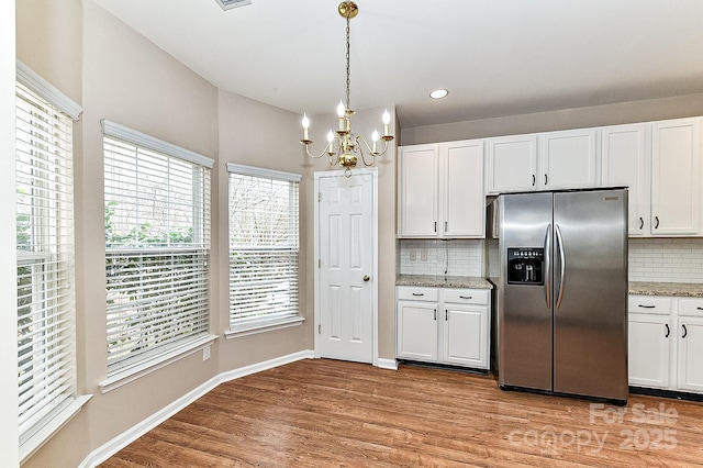 kitchen with light stone counters, stainless steel fridge with ice dispenser, and white cabinets