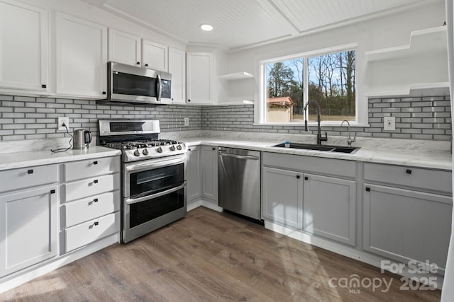 kitchen with sink, white cabinetry, stainless steel appliances, dark wood-type flooring, and light stone countertops