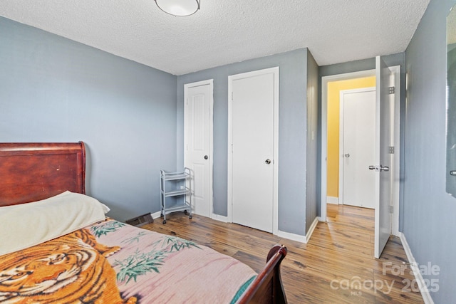 bedroom featuring light wood-type flooring, a textured ceiling, and two closets