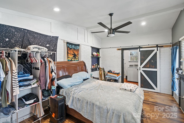 bedroom featuring vaulted ceiling, wood-type flooring, washer / dryer, brick wall, and a barn door