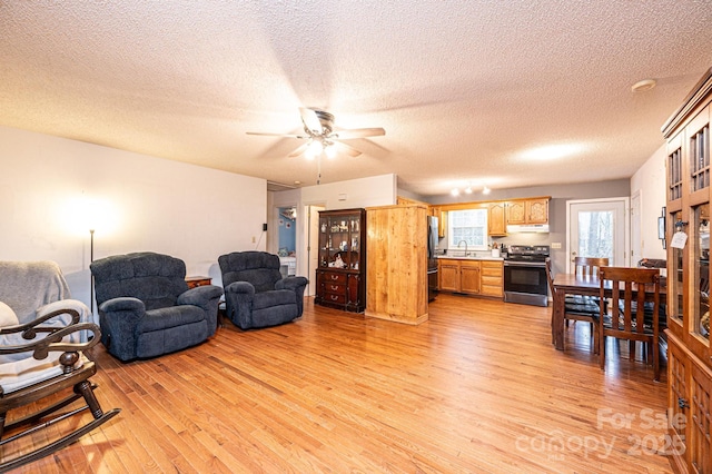 living room featuring ceiling fan, sink, light hardwood / wood-style floors, and a textured ceiling