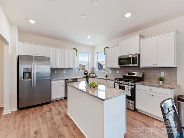 kitchen featuring appliances with stainless steel finishes, light hardwood / wood-style flooring, a kitchen island, white cabinets, and light stone countertops