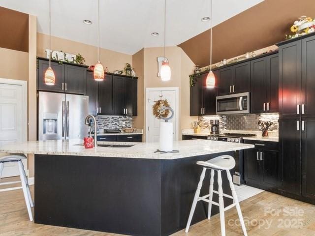 kitchen featuring appliances with stainless steel finishes, a kitchen bar, a kitchen island with sink, and pendant lighting