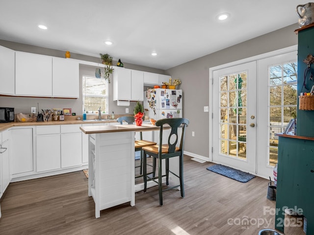 kitchen with white cabinetry, white refrigerator, a breakfast bar area, and hardwood / wood-style flooring