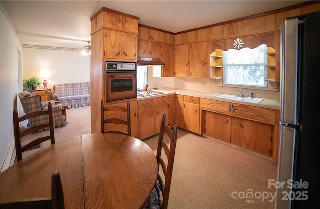 kitchen featuring oven, light countertops, a wealth of natural light, freestanding refrigerator, and a sink