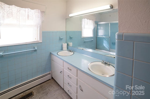 bathroom with a sink, tile walls, a stall shower, and a baseboard radiator