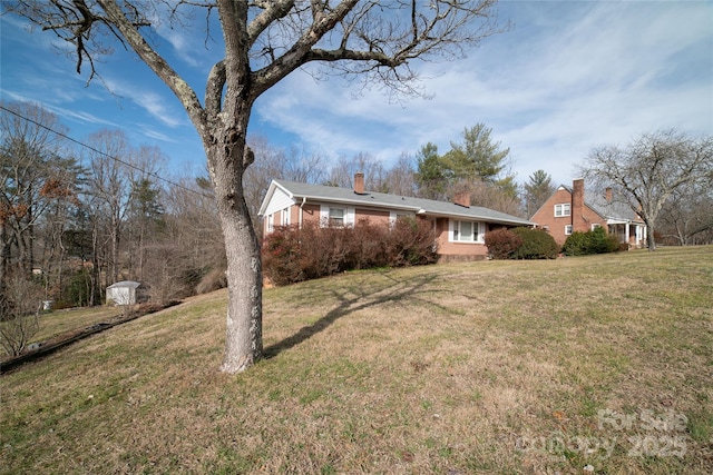 view of side of home with a yard, brick siding, and a chimney