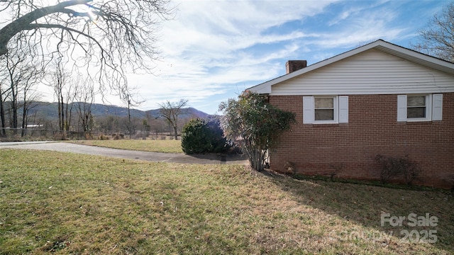 view of property exterior featuring a mountain view, brick siding, a chimney, and a lawn