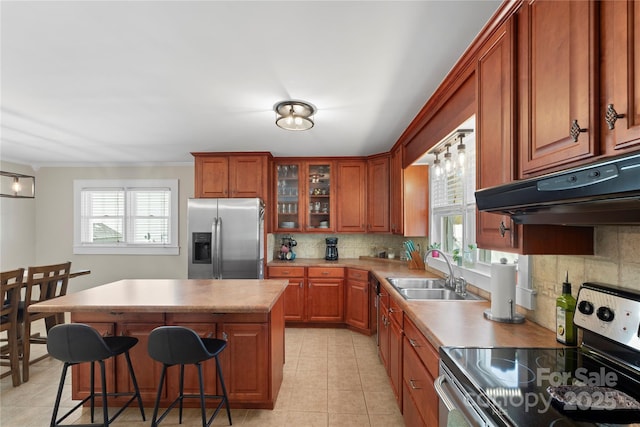 kitchen featuring under cabinet range hood, appliances with stainless steel finishes, brown cabinetry, and a sink