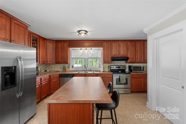 kitchen with a breakfast bar, a sink, under cabinet range hood, stainless steel appliances, and decorative backsplash