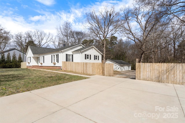 view of home's exterior featuring a shingled roof, a lawn, concrete driveway, and fence