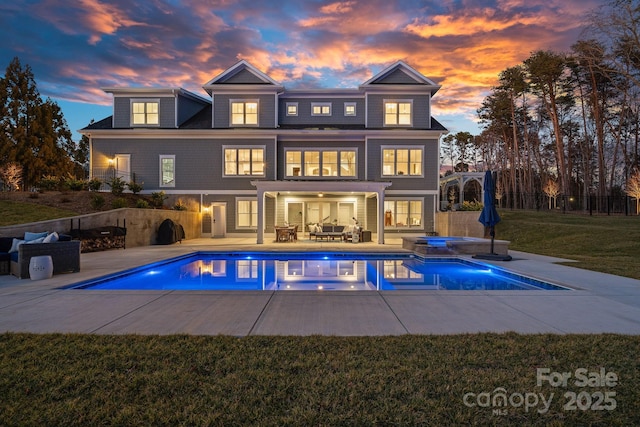 back of house at dusk featuring a patio, a yard, and a pool with connected hot tub